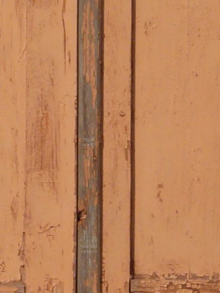 Light brown window texture, with rough, worn painted shutters closed over it. Green hues are visible in the wood frame, and a ledge sits over the window.