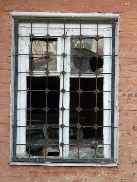 White window texture with chipping paint and missing panes, with a grid of iron bars set over it. The window is set in a brick wall painted red.