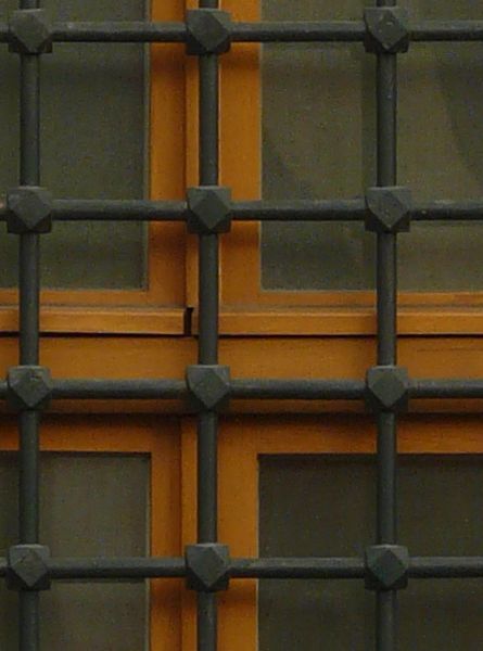 Brown window texture, with heavy black iron bars gridded across it, and set in a red and white brick wall. A small half-circle window sits separately at the top.