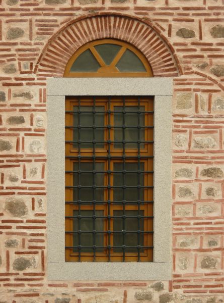 Brown window texture, with heavy black iron bars gridded across it, and set in a red and white brick wall. A small half-circle window sits separately at the top.