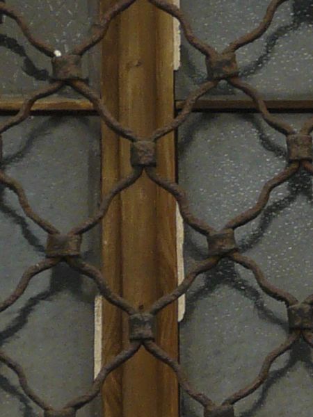Arched window texture with golden brown trim and a heavy iron lattice set over it. It is recessed into a tan stone wall.