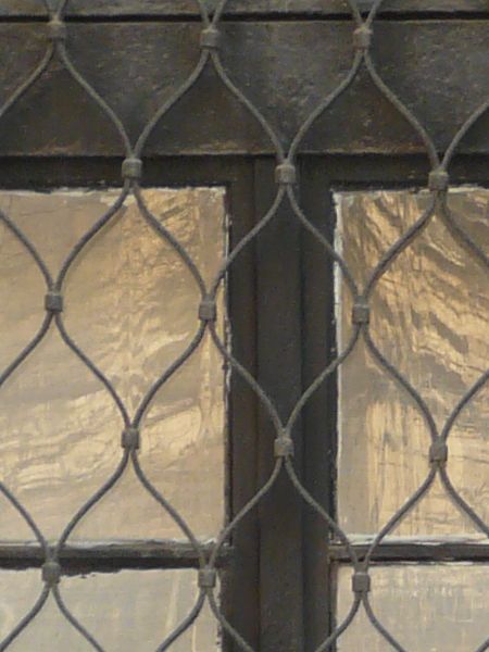 Arched window texture with dark brown trim and a curved iron lattice set over it. The window is set in a wall of red brick and tan mortar.