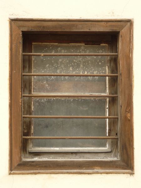 Wooden window texture, with rusted iron bars running laterally across it. The glass is clouded and covered with scratches and white marks.