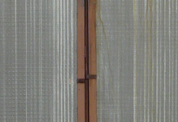 Clouded windows texture, with brown wood separating the tall panes. Crossed boards are visible behind the windows.