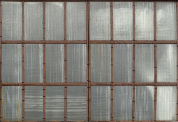 Clouded windows texture, with brown wood separating the tall panes. Crossed boards are visible behind the windows.