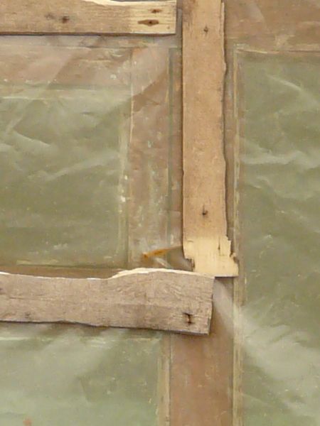Plastic covered window texture, with scraps of brown and blue painted wood within the frame. The window is recessed in a red brick wall.