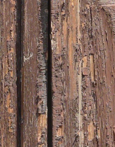 Rough brown window texture, closed by shutters made of broken, leaning and extremely worn wood. White brick surrounds the window.