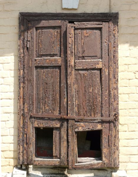Rough brown window texture, closed by shutters made of broken, leaning and extremely worn wood. White brick surrounds the window.
