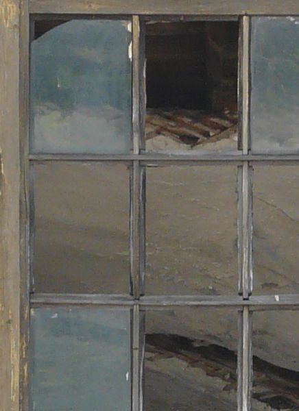 Arched window texture with yellow wood separating the panes, several of which are missing. A whitewashed wall surrounds the window, and large pieces of wood are visible behind it.