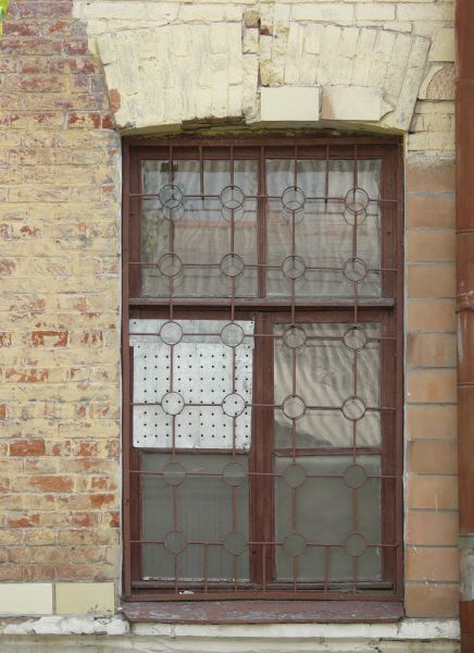 Window texture with red bars formed in a grid and circle pattern over the panes. A white board full of holes covers one pane, and the window is set in a brick wall in various shades of red and yellow.