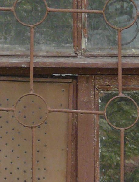 Window texture with red bars formed in a grid and circle pattern over the panes. A white board full of holes covers one pane, and the window is set in a brick wall in various shades of red and yellow.