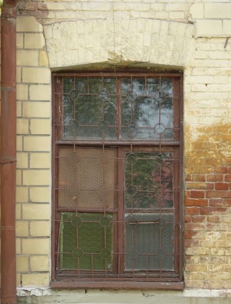 Window texture with red bars formed in a grid and circle pattern over the panes. A white board full of holes covers one pane, and the window is set in a brick wall in various shades of red and yellow.