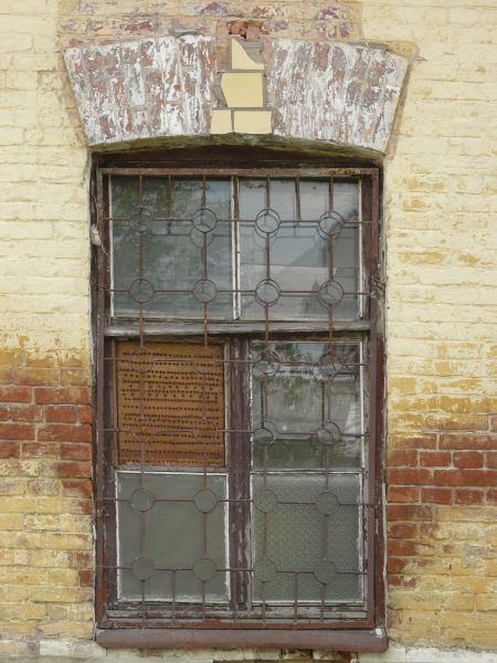 Window texture with red bars formed in a grid and circle pattern over the panes. A white board full of holes covers one pane, and the window is set in a brick wall in various shades of red and yellow.