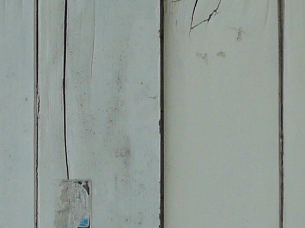 Large white window texture, closed by shutters made up of cracked and broken boards and set in an eroding stone wall. A strip of thin metal runs across the top.