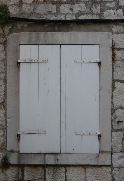 White windwo texture closed by shutters with vertical cracks, and framed by grey stone and brick.