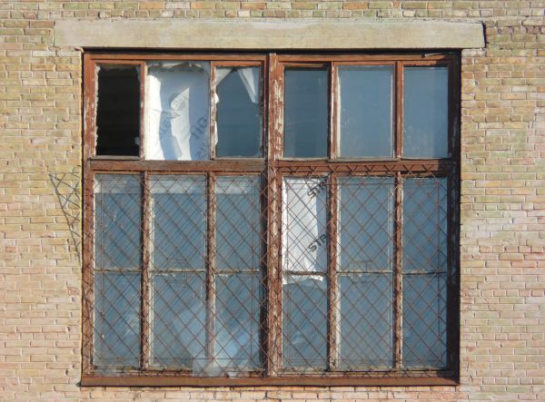 Window texture with panes divided by rusted metal, and partially covered by a rusted metal lattice. White material is visible behind some of the panes, and a white tube is protruding from one of them.