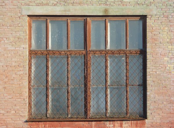 Window texture with panes divided by rusted metal, and partially covered by a rusted metal lattice. White material is visible behind some of the panes, and a white tube is protruding from one of them.