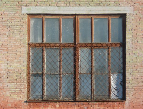 Window texture with panes divided by rusted metal, and partially covered by a rusted metal lattice. White material is visible behind some of the panes, and a white tube is protruding from one of them.