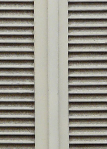 Window texture, with white shutters closed over it and set within a worn stone frame with a large ledge at the top.