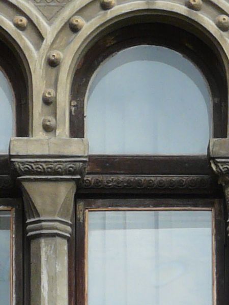 Tall arched window texture, with three vertical panes that each have a curved top edge. The wall and frame that surround them are of elaborately patterned brick and stone.