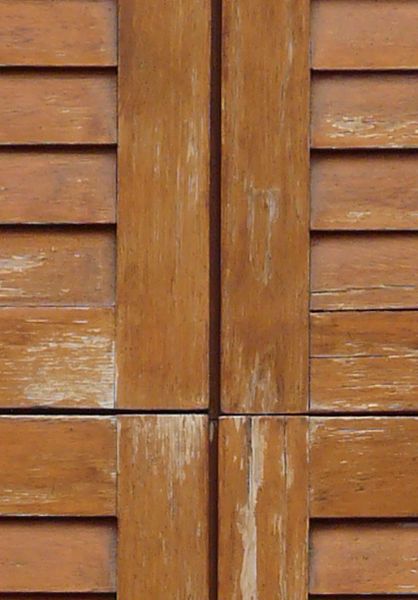 Window texture featuring a brown wooden frame with a triangular top, and worn wooden shutters closed over it.