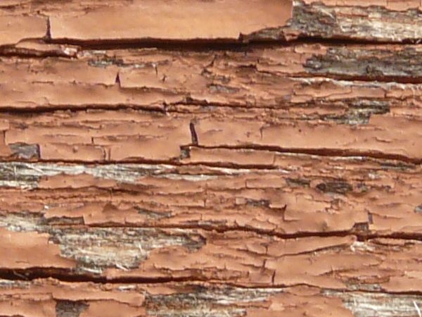 Old red wood texture, with heavy cracking and chipping, and some areas of grey wood visible underneath.