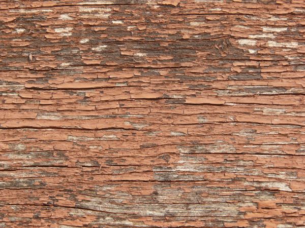 Old red wood texture, with heavy cracking and chipping, and some areas of grey wood visible underneath.