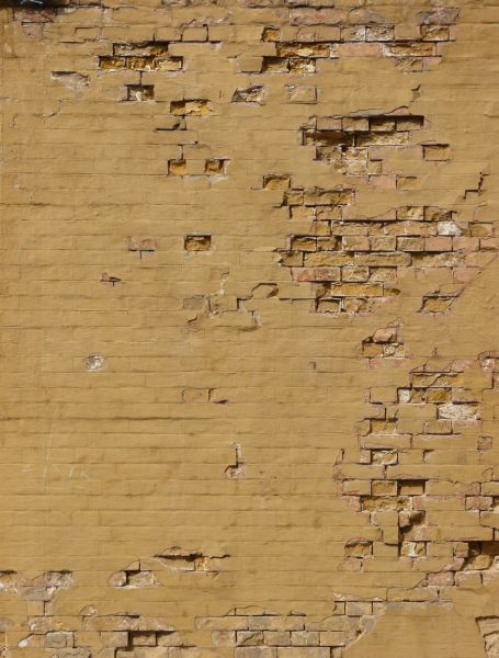 Texture of brick wall painted over in brown paint. Surface is very worn and damaged.