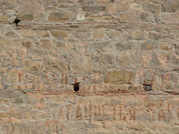 Stone wall in beige tone with red graffiti on smooth surface.