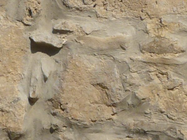 Stone wall in beige tone with red graffiti on smooth surface.