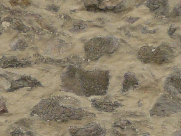 Medieval stone wall of grey stones of various shapes in thick, beige concrete.