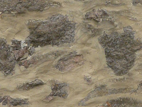 Medieval stone wall of grey stones of various shapes in thick, beige concrete.