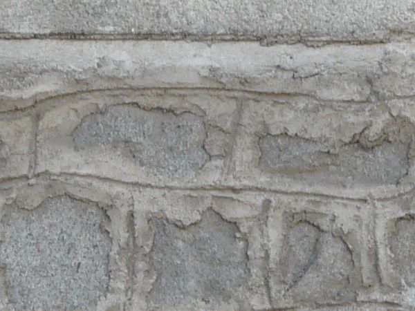 Uneven grey brick wall texture, set under an area of solid grey stone. Markings have been traced in the cement that separates the bricks.