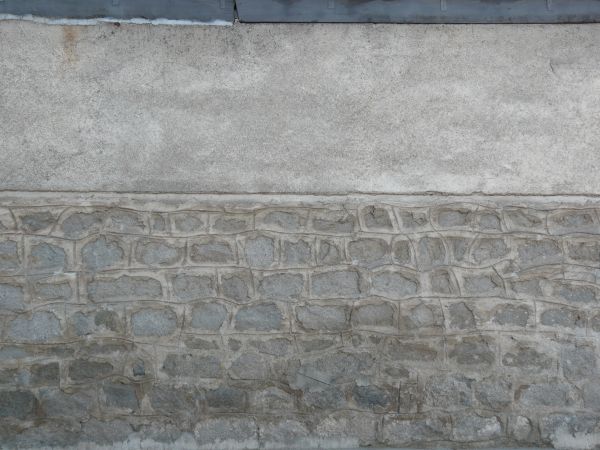 Uneven grey brick wall texture, set under an area of solid grey stone. Markings have been traced in the cement that separates the bricks.