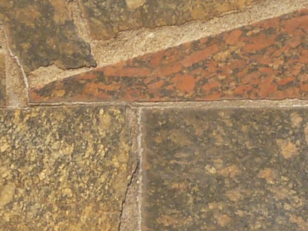 Pavement consisting of stone slate cut in pieces of random shapes and set in brown cement.