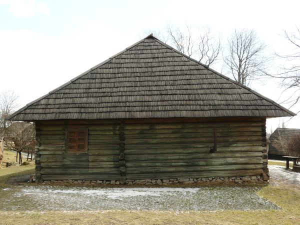 Small, wooden cabin with log walls and roof made of wooden shingles.