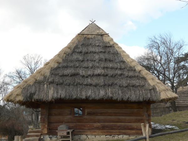 Small cabin made of large, wooden logs with tall, thatched roof.