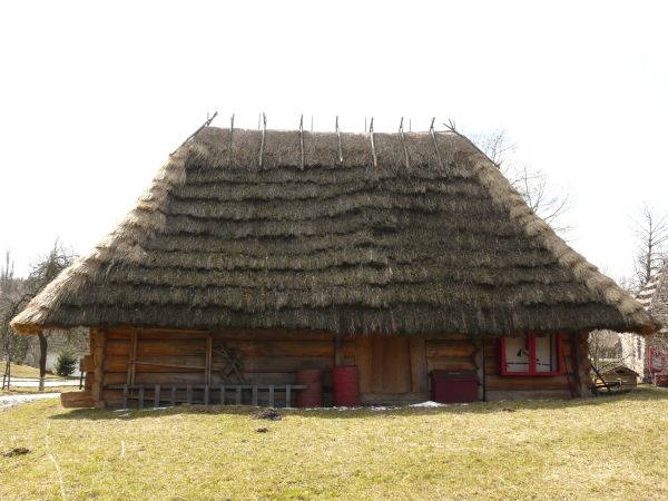 Small cabin made of large, wooden logs with tall, thatched roof.