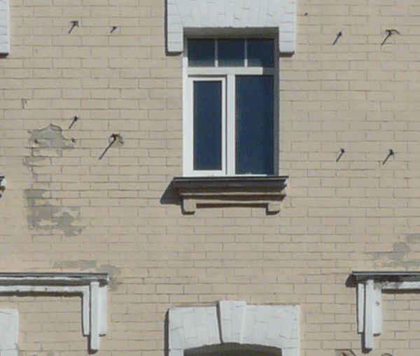Building fa��ade of beige and white brick with gable roof and very worn surface.
