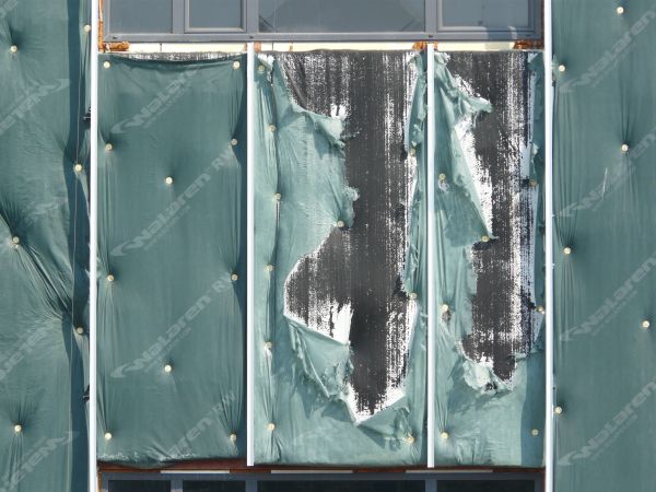 Wall texture, covered by pieces of thin green plastic divided by thin white strips. A worn black surface is visible behind some of the plastic.