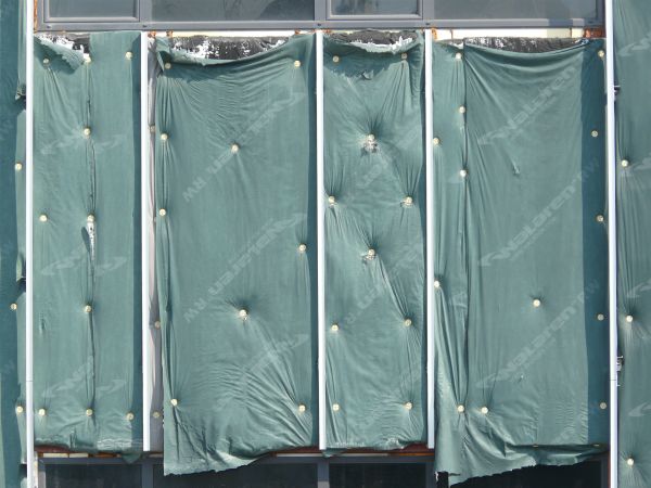 Wall texture, covered by pieces of thin green plastic divided by thin white strips. A worn black surface is visible behind some of the plastic.