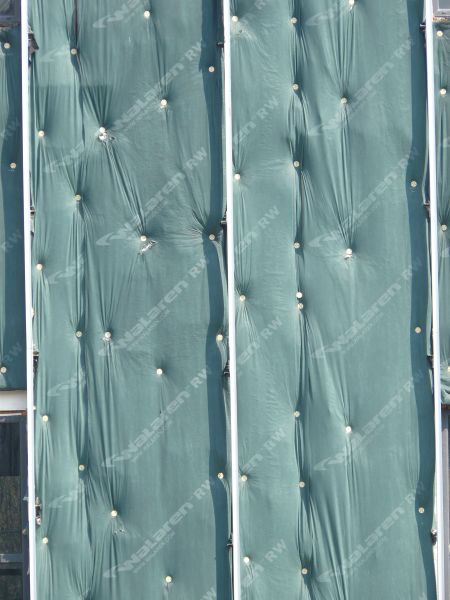 Wall texture, covered by pieces of thin green plastic divided by thin white strips. A worn black surface is visible behind some of the plastic.