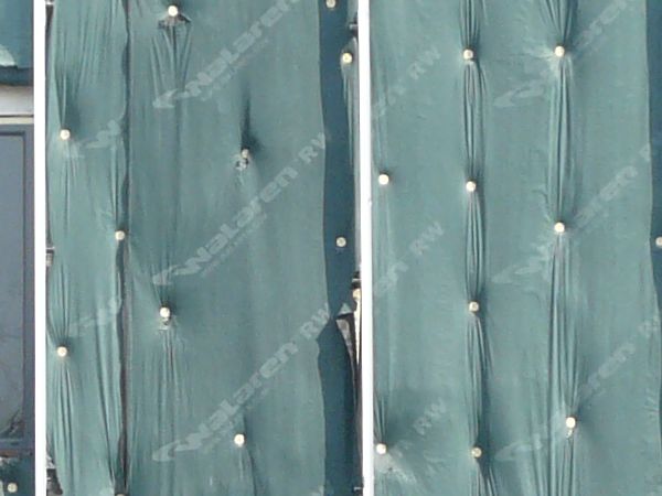 Wall texture, covered by pieces of thin green plastic divided by thin white strips. A worn black surface is visible behind some of the plastic.