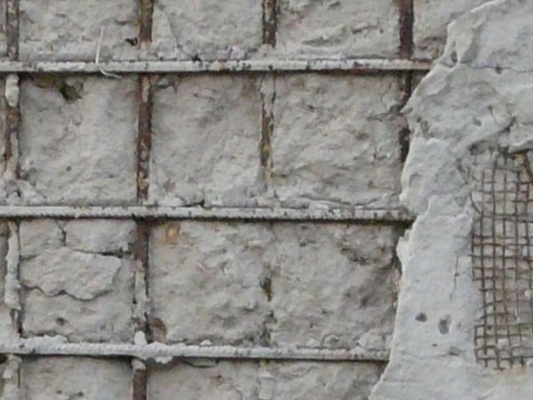Concrete texture with graffiti and very damaged surface exposing iron rebar and mesh.