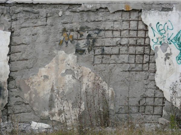 Concrete texture with graffiti and very damaged surface exposing iron rebar and mesh.