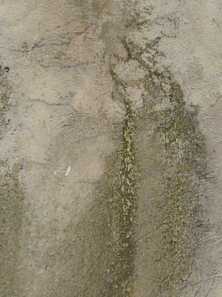 Texture of rough, irregular concrete in beige tone with dark streak coming from pipe.