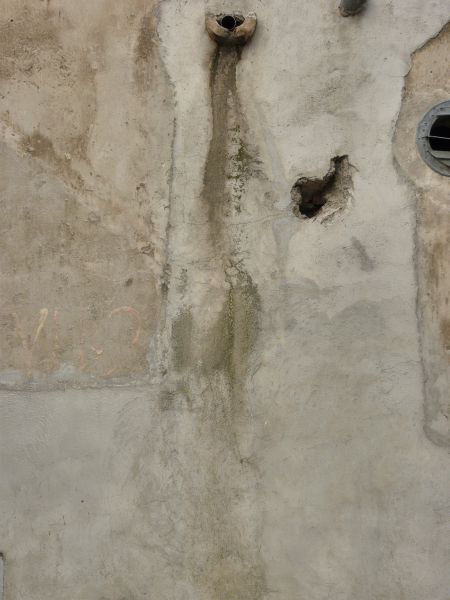 Texture of rough, irregular concrete in beige tone with dark streak coming from pipe.