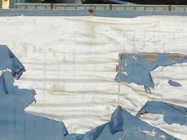 Texture of tall fence with worn, torn plastic covering on bottom.