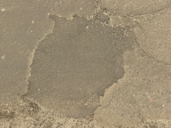 Road texture with dark areas of asphalt patching holes, thin crack extending from the patches, and a small, unfilled hole.