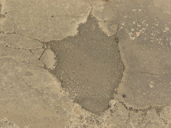 Road texture with dark areas of asphalt patching holes, thin crack extending from the patches, and a small, unfilled hole.